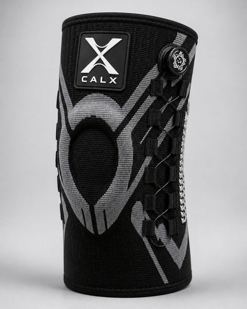 A black and gray CALX knee support sleeve with a black logo patch on the front and a side adjustment dial, shown on a neutral gray background.
